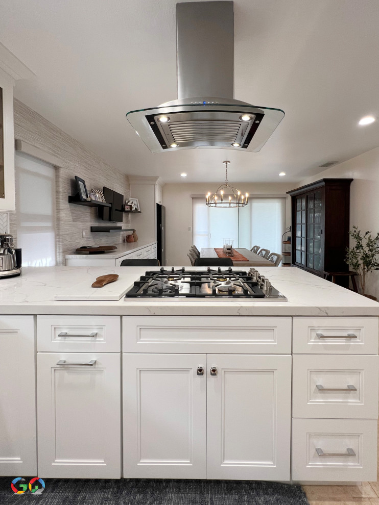 This is an example of an expansive modern l-shaped eat-in kitchen in Orange County with a farmhouse sink, shaker cabinets, white cabinets, quartzite benchtops, grey splashback, ceramic splashback, stainless steel appliances, ceramic floors, a peninsula, beige floor and white benchtop.