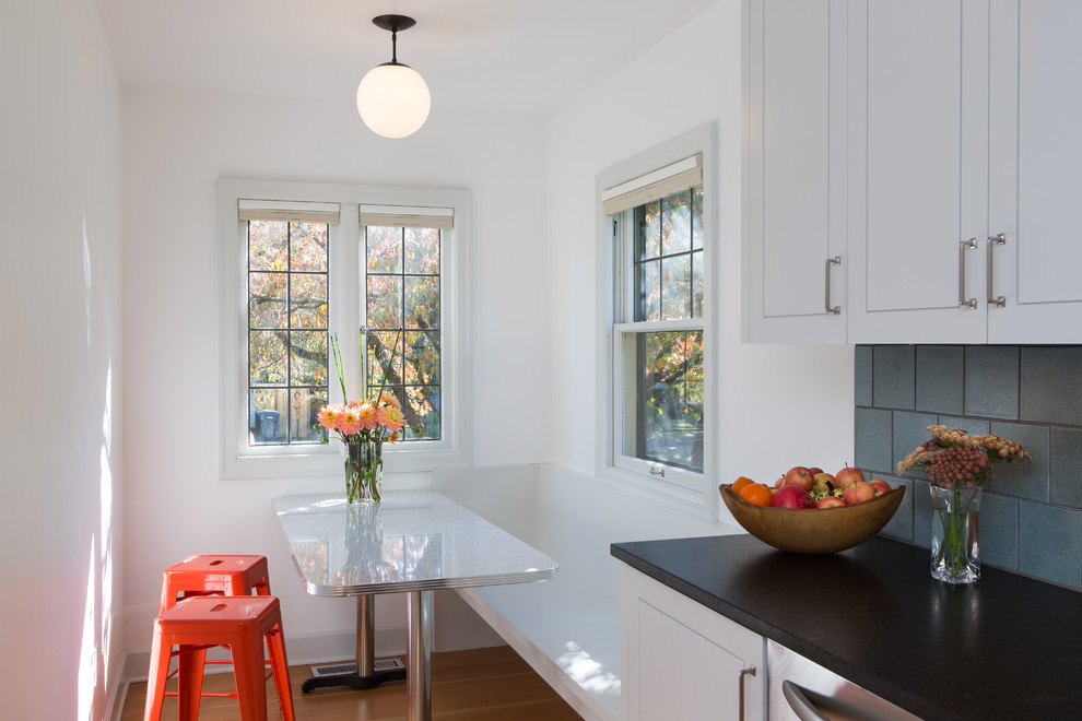 This is an example of a small transitional u-shaped kitchen in Portland with a farmhouse sink, white cabinets, granite benchtops, blue splashback, ceramic splashback, stainless steel appliances and light hardwood floors.