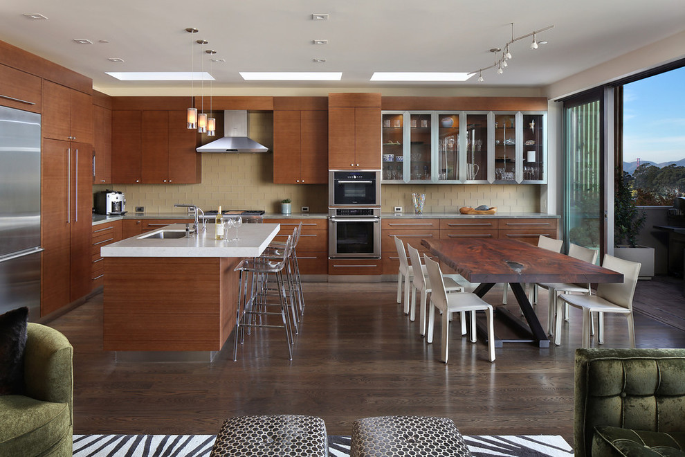 This is an example of a large contemporary l-shaped open plan kitchen in San Francisco with an undermount sink, flat-panel cabinets, medium wood cabinets, beige splashback, glass tile splashback, stainless steel appliances, dark hardwood floors, with island, quartz benchtops and brown floor.
