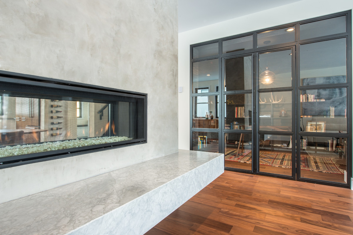 This is an example of a contemporary study room with black walls, medium hardwood floors, a two-sided fireplace, a concrete fireplace surround and a freestanding desk.