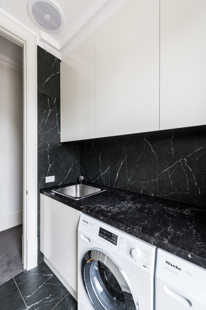 Large contemporary galley dedicated laundry room in Melbourne with a drop-in sink, flat-panel cabinets, beige cabinets, quartz benchtops, black walls, porcelain floors, a side-by-side washer and dryer and black floor.
