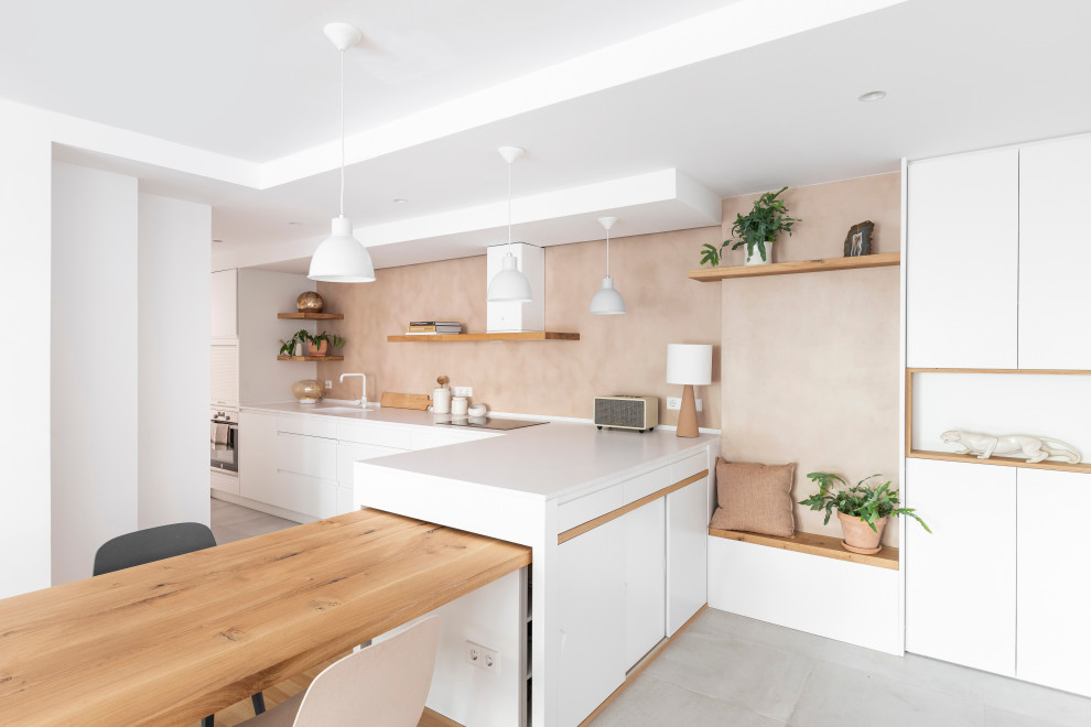 Design ideas for a scandinavian l-shaped eat-in kitchen in Barcelona with an undermount sink, flat-panel cabinets, white cabinets, beige splashback, stainless steel appliances, a peninsula, grey floor and white benchtop.