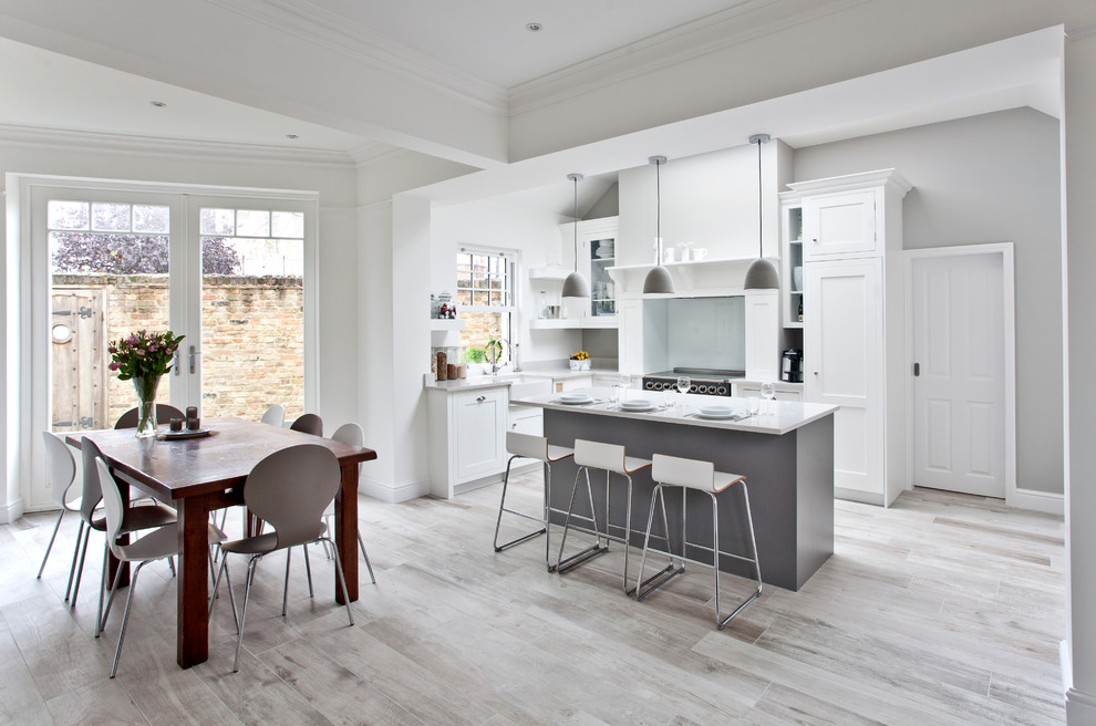 Photo of a large transitional l-shaped eat-in kitchen in Surrey with a farmhouse sink, shaker cabinets, grey cabinets, solid surface benchtops, grey splashback, glass sheet splashback, stainless steel appliances, light hardwood floors and with island.