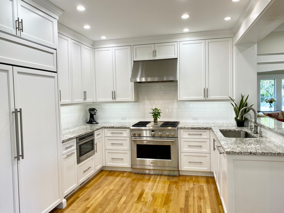 Design ideas for a large transitional u-shaped eat-in kitchen in Tampa with an undermount sink, shaker cabinets, white cabinets, granite benchtops, white splashback, subway tile splashback, stainless steel appliances, light hardwood floors, with island, beige floor and multi-coloured benchtop.