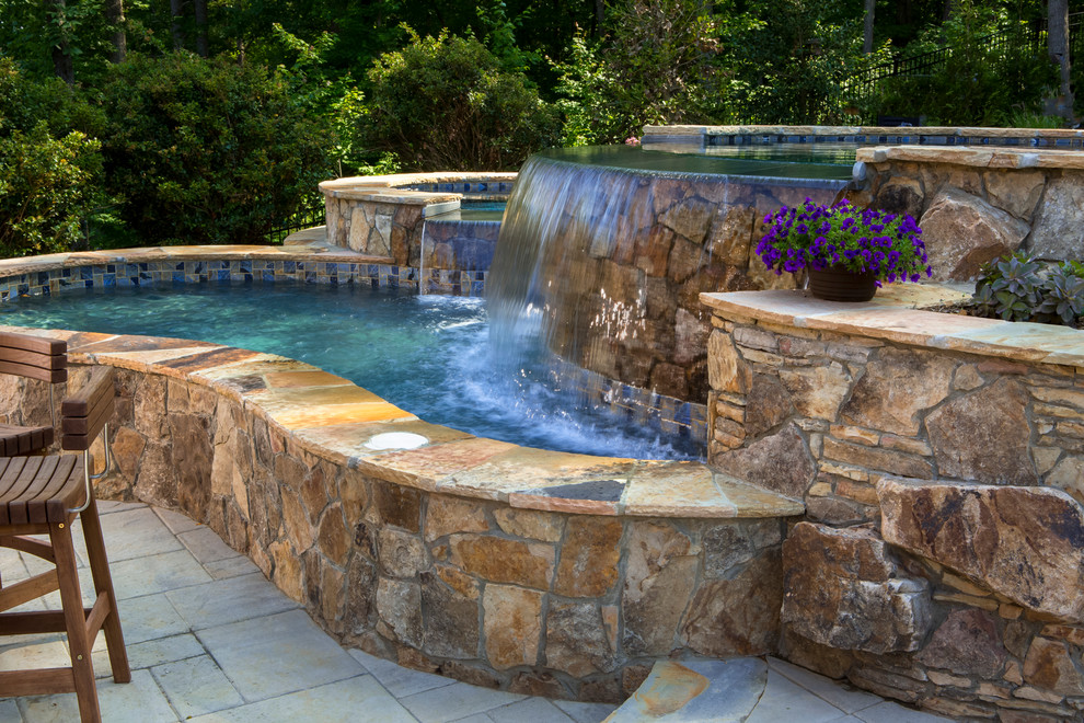 Large tropical backyard custom-shaped natural pool in Charlotte with a water feature and concrete pavers.