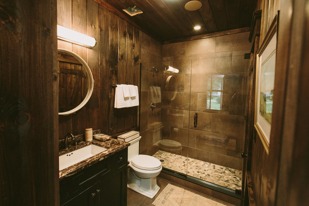 This is an example of a mid-sized country 3/4 bathroom in Baltimore with recessed-panel cabinets, dark wood cabinets, an alcove shower, a two-piece toilet, gray tile, stone tile, brown walls, travertine floors, an undermount sink and soapstone benchtops.