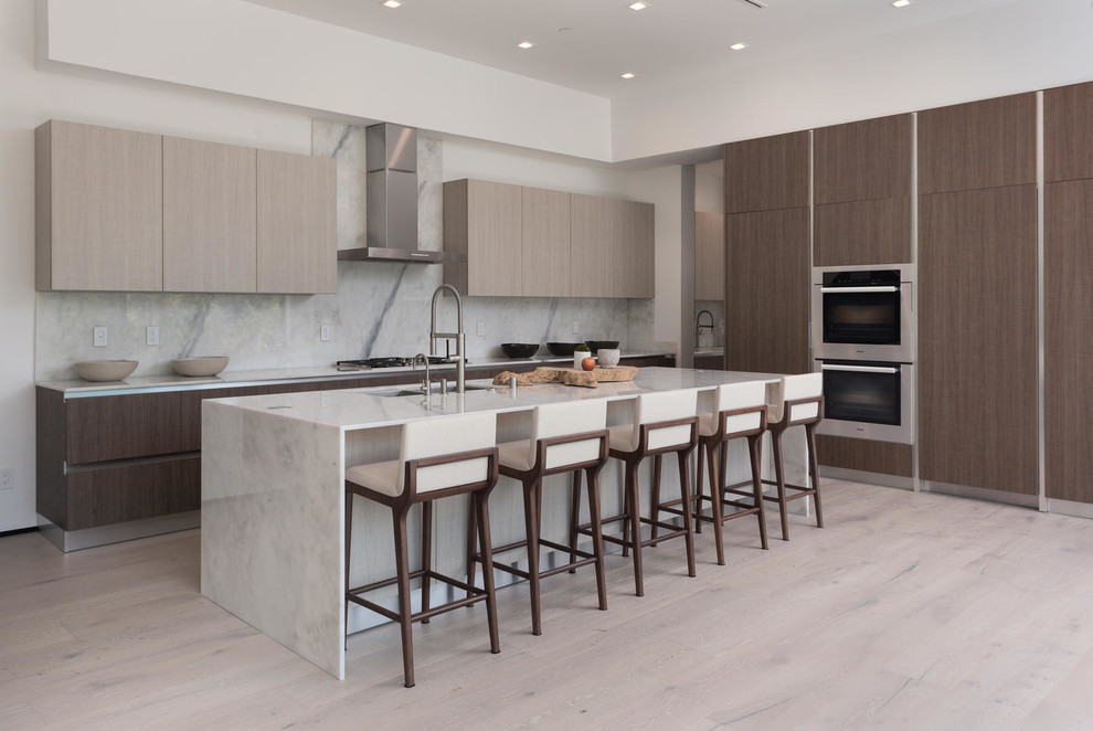 This is an example of a large modern single-wall open plan kitchen in Los Angeles with a single-bowl sink, flat-panel cabinets, light wood cabinets, marble benchtops, white splashback, stone slab splashback, stainless steel appliances, light hardwood floors and with island.