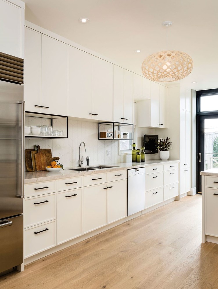 Design ideas for a large contemporary galley open plan kitchen in San Francisco with white cabinets, white splashback, stainless steel appliances, a double-bowl sink, shaker cabinets, solid surface benchtops, porcelain splashback and light hardwood floors.