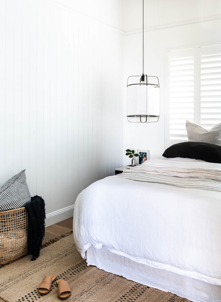 This is an example of a beach style bedroom in Brisbane with white walls, medium hardwood floors and brown floor.