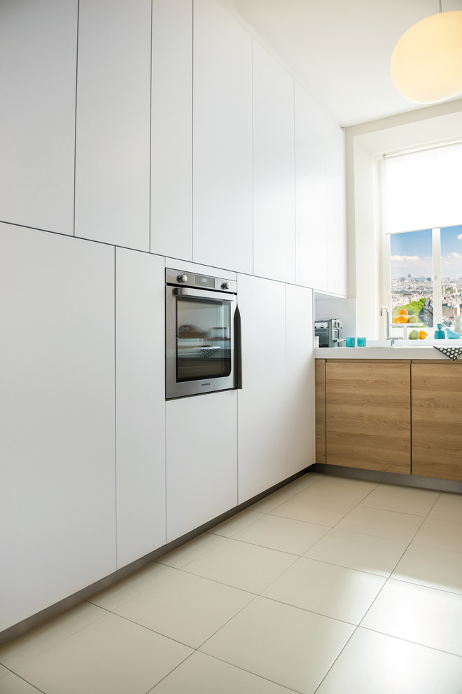 This is an example of a small contemporary l-shaped kitchen in London with a single-bowl sink, white splashback, glass sheet splashback, stainless steel appliances, ceramic floors and light wood cabinets.