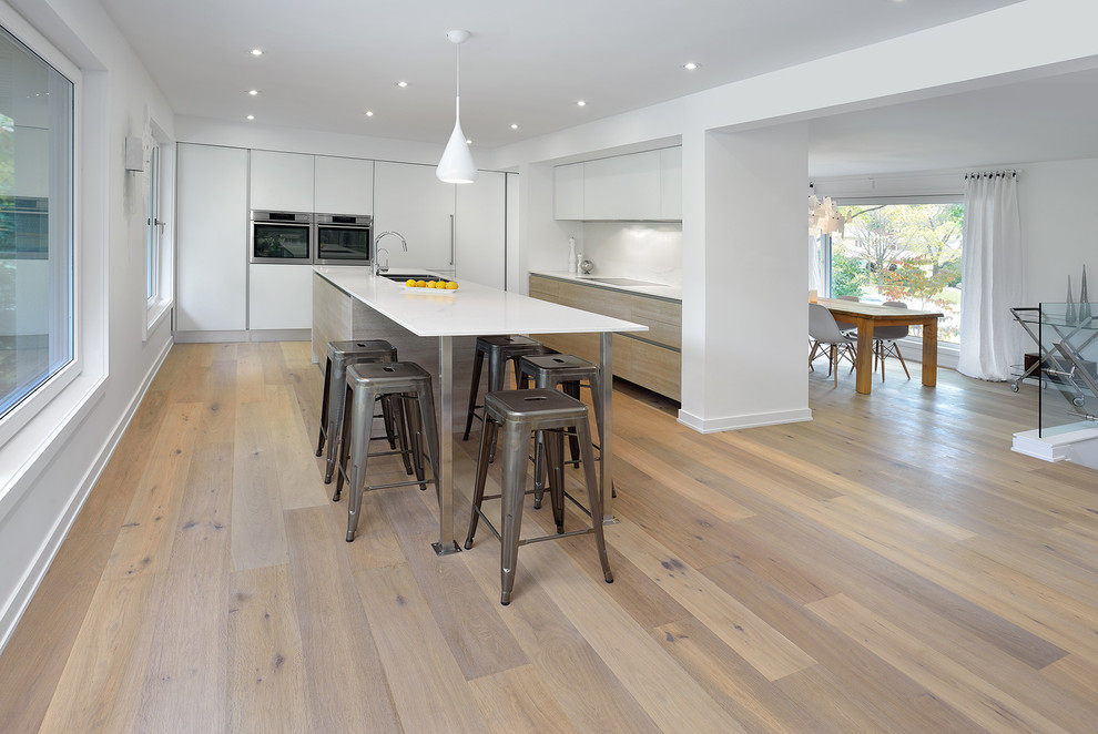 This is an example of a mid-sized contemporary l-shaped kitchen in Toronto with flat-panel cabinets, white cabinets, stainless steel appliances, light hardwood floors and with island.