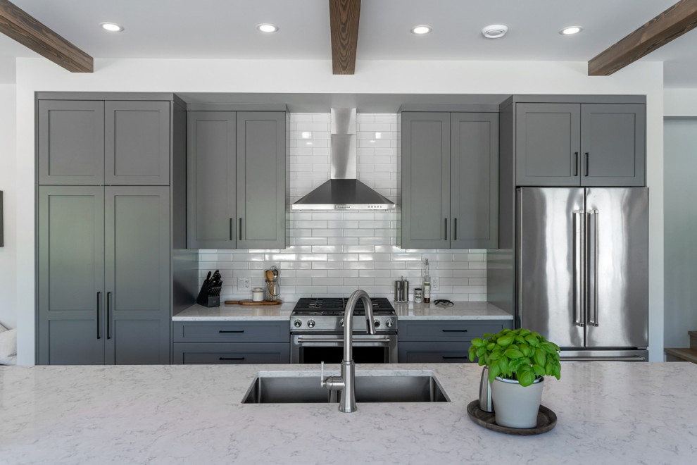 Inspiration for a mid-sized transitional single-wall light wood floor, brown floor and exposed beam eat-in kitchen remodel with an undermount sink, shaker cabinets, gray cabinets, quartzite countertops, white backsplash, subway tile backsplash, stainless steel appliances, an island and multicolored countertops