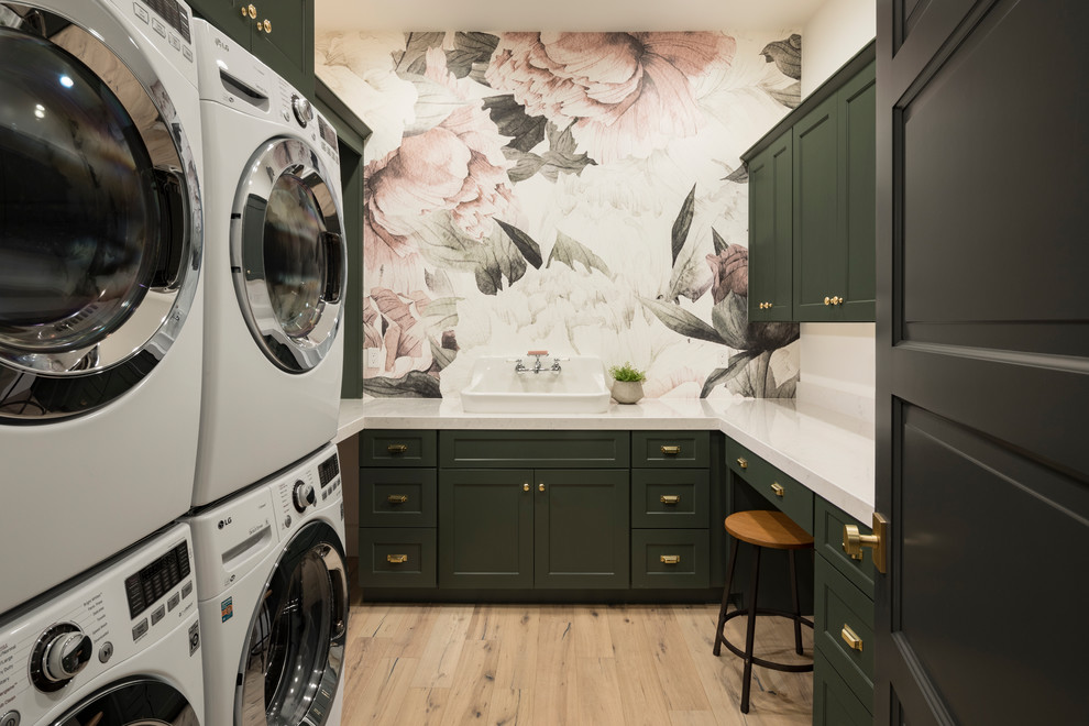 This is an example of a large transitional u-shaped dedicated laundry room in Phoenix with shaker cabinets, green cabinets, multi-coloured walls, light hardwood floors, quartz benchtops, a stacked washer and dryer, beige floor, white benchtop and a drop-in sink.