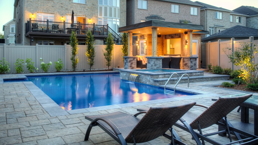 This is an example of a mid-sized traditional backyard rectangular natural pool in Toronto with natural stone pavers.