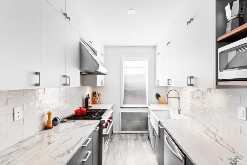 Inspiration for a small modern u-shaped eat-in kitchen with a farmhouse sink, flat-panel cabinets, white cabinets, marble benchtops, white splashback, ceramic splashback, stainless steel appliances, painted wood floors, grey floor and white benchtop.