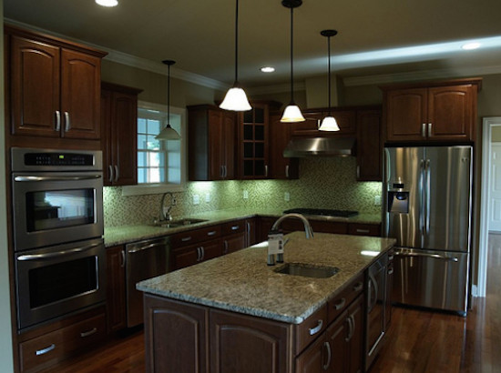 Inspiration for a transitional medium tone wood floor kitchen remodel in Nashville with an undermount sink, dark wood cabinets, granite countertops, mosaic tile backsplash, stainless steel appliances, an island and raised-panel cabinets