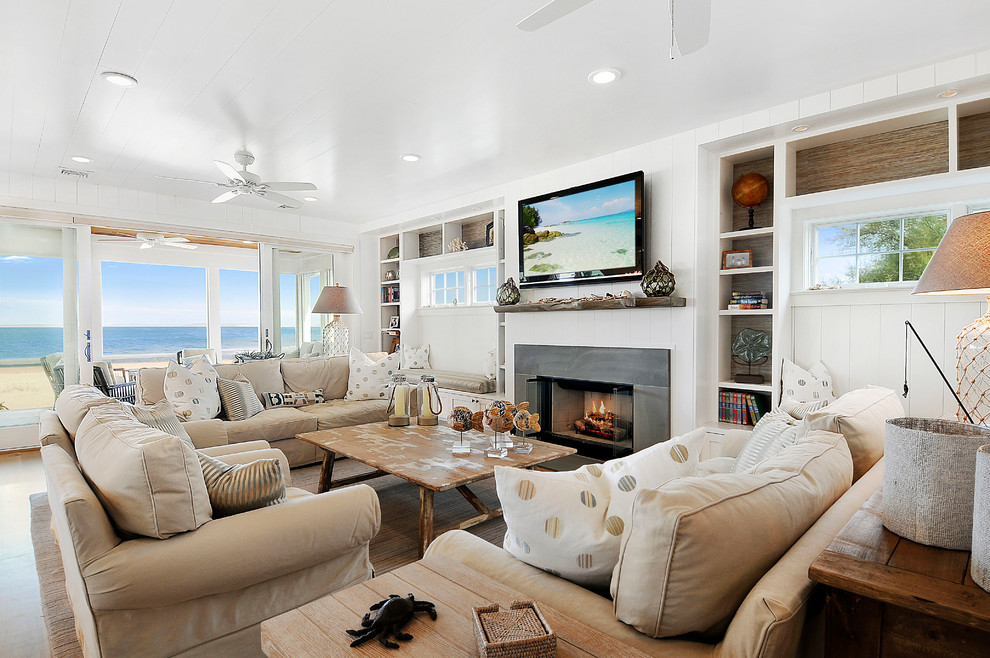This is an example of a mid-sized beach style open concept family room in Other with white walls, light hardwood floors, a standard fireplace, a wall-mounted tv and a stone fireplace surround.