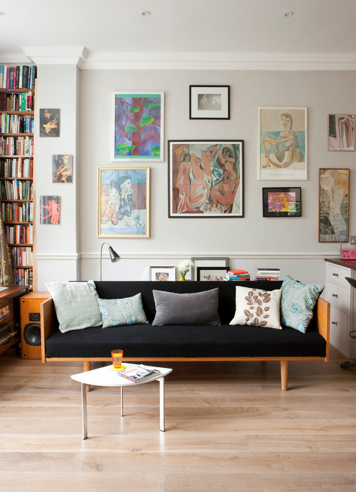 This is an example of an eclectic open concept living room in London with beige walls and light hardwood floors.