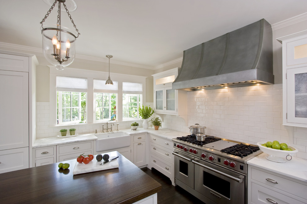 Large traditional u-shaped eat-in kitchen in New York with a farmhouse sink, wood benchtops, beaded inset cabinets, white cabinets, white splashback, ceramic splashback, dark hardwood floors, with island and stainless steel appliances.