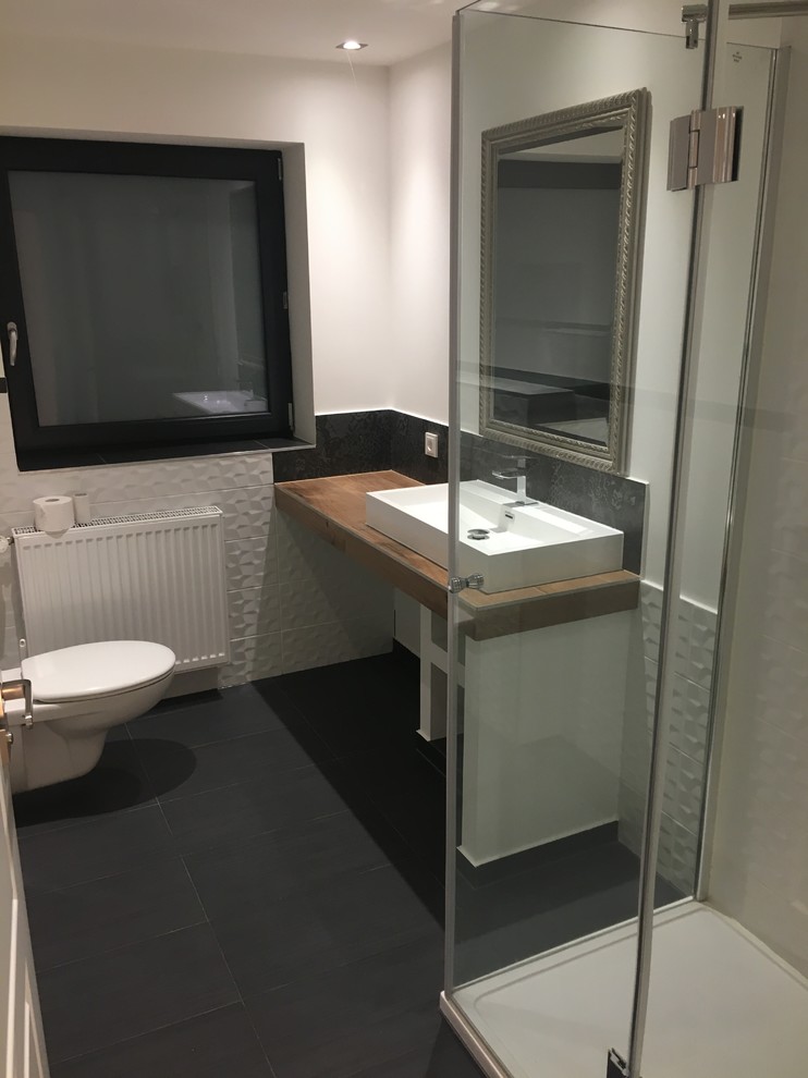 This is an example of a small contemporary 3/4 bathroom in Other with a corner shower, a wall-mount toilet, black and white tile, ceramic tile, white walls, cement tiles, a vessel sink, wood benchtops, black floor and a hinged shower door.