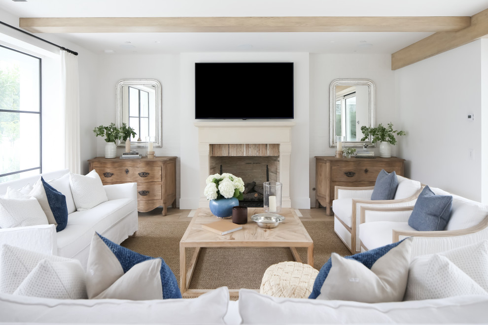 This is an example of a beach style living room in Orange County with white walls, light hardwood floors, a standard fireplace, a wall-mounted tv and beige floor.