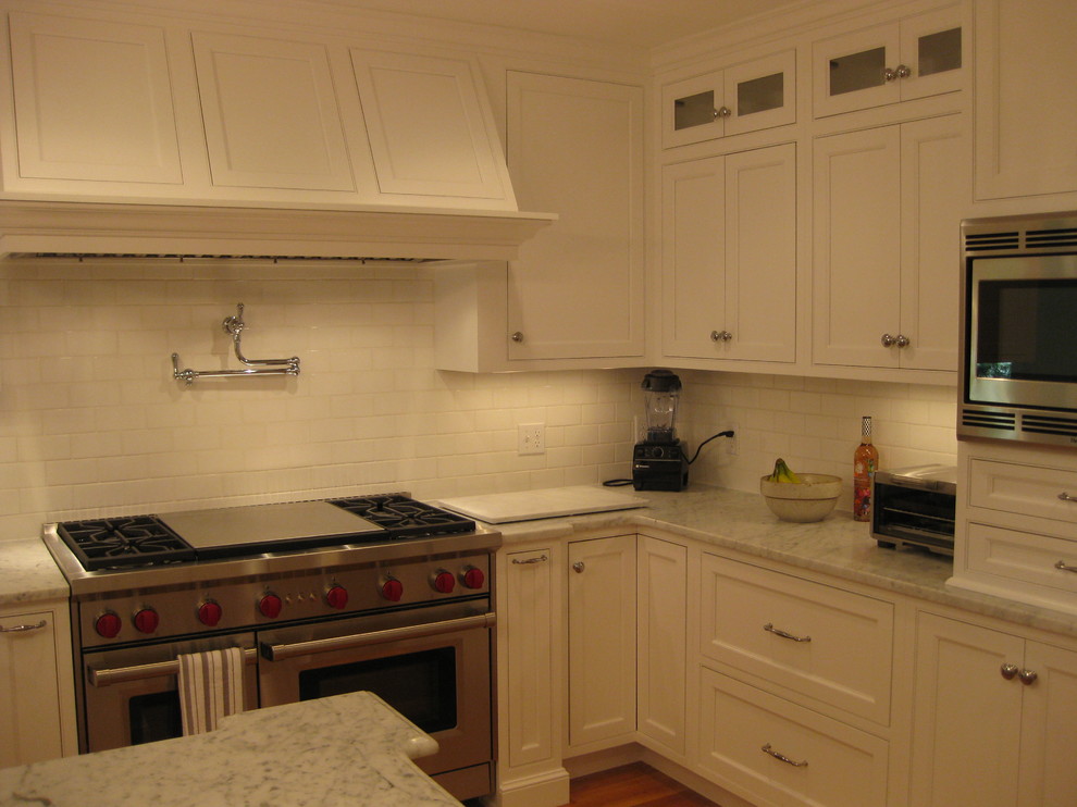 Inspiration for a transitional u-shaped medium tone wood floor eat-in kitchen remodel in Boston with a farmhouse sink, beaded inset cabinets, white cabinets, marble countertops, white backsplash, subway tile backsplash, stainless steel appliances and an island