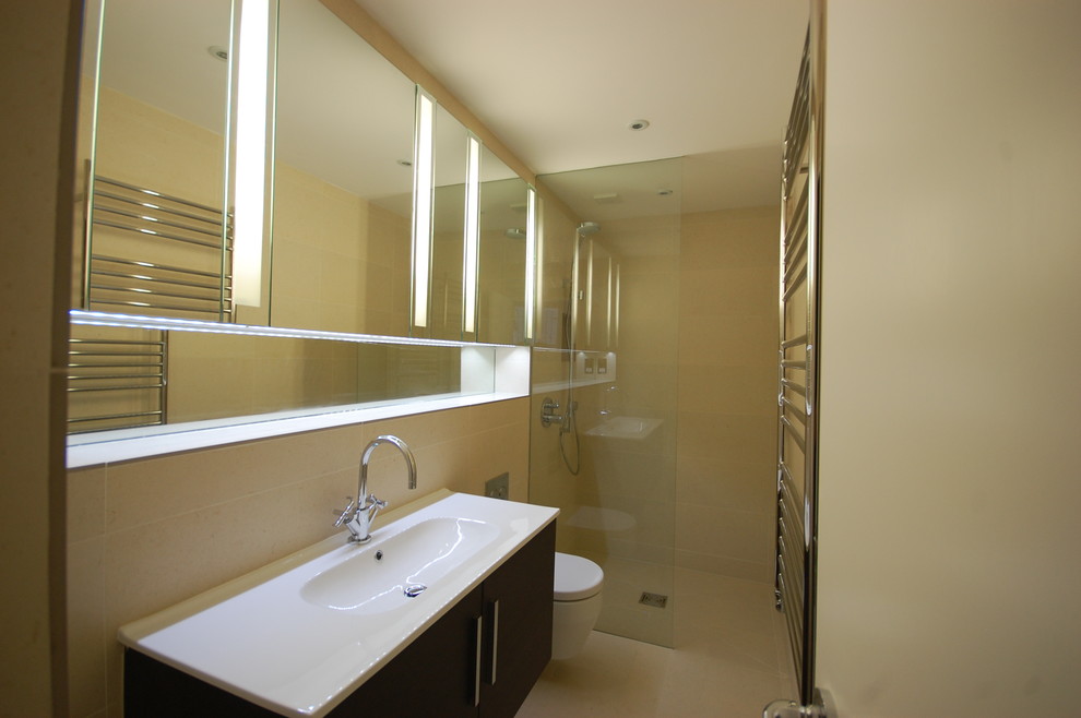 Photo of a small contemporary 3/4 bathroom in London with a drop-in sink, flat-panel cabinets, medium wood cabinets, an open shower, a wall-mount toilet, black tile, porcelain tile, beige walls and porcelain floors.