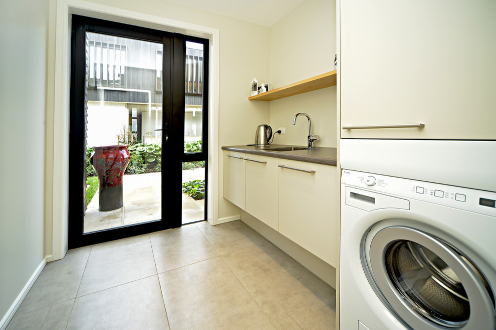 Inspiration for a mid-sized contemporary galley dedicated laundry room in Auckland with an undermount sink, flat-panel cabinets, beige cabinets, laminate benchtops, white walls, ceramic floors and a stacked washer and dryer.