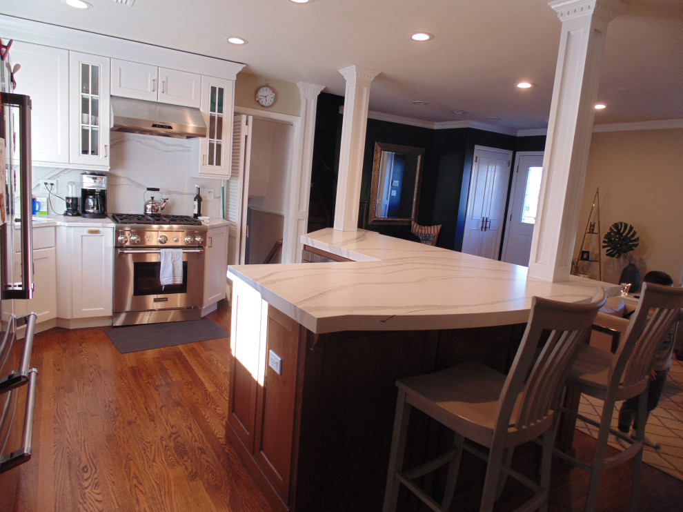 Mid-sized transitional u-shaped medium tone wood floor and brown floor eat-in kitchen photo with an undermount sink, recessed-panel cabinets, white cabinets, quartz countertops, white backsplash, stone slab backsplash, stainless steel appliances, no island and white countertops
