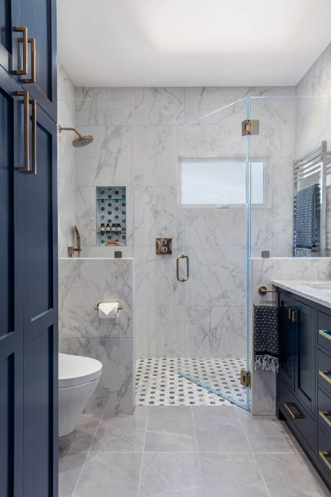 This is an example of a mid-sized transitional master bathroom in San Francisco with shaker cabinets, blue cabinets, a curbless shower, a wall-mount toilet, white tile, porcelain tile, white walls, marble floors, an undermount sink, engineered quartz benchtops, multi-coloured floor, a hinged shower door, white benchtops, a shower seat, a double vanity and a freestanding vanity.