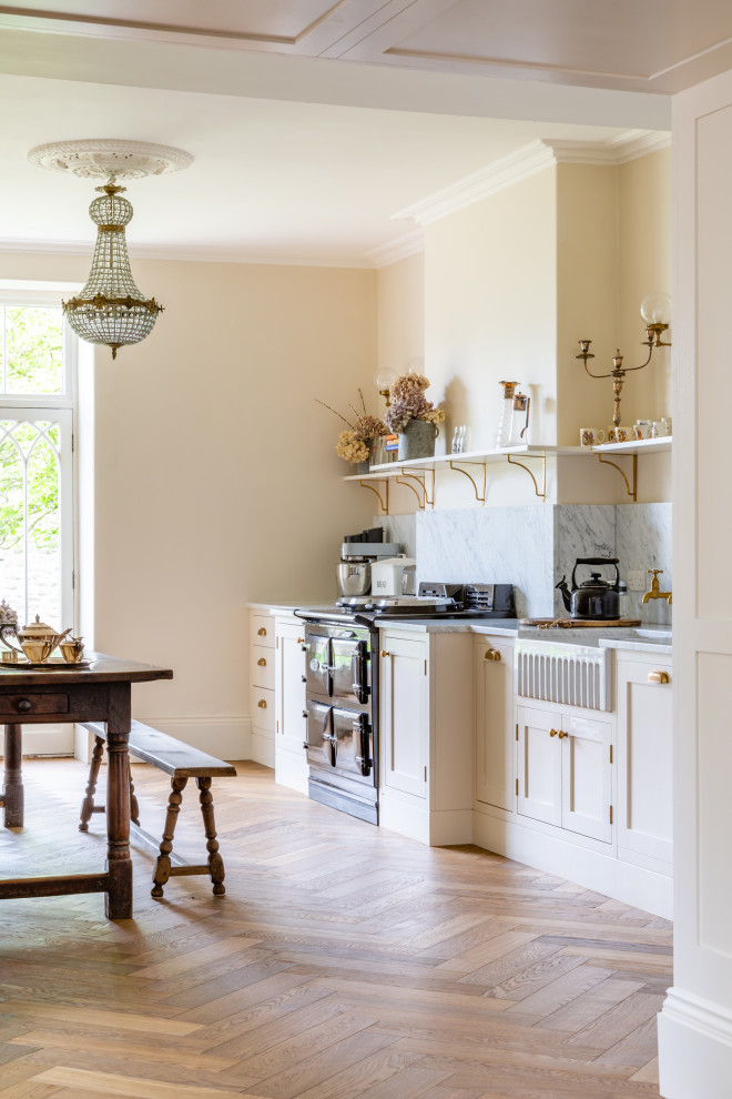 Bild på ett stort vintage vit vitt kök och matrum, med en rustik diskho, skåp i shakerstil, beige skåp, marmorbänkskiva, vitt stänkskydd, stänkskydd i marmor, svarta vitvaror, mellanmörkt trägolv och brunt golv