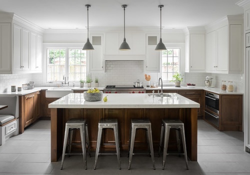 Two-tone kitchen with white upper cabinets, rich wood lower cabinets, marble island, and metal bar stools under pendant lights — modern yet warm design