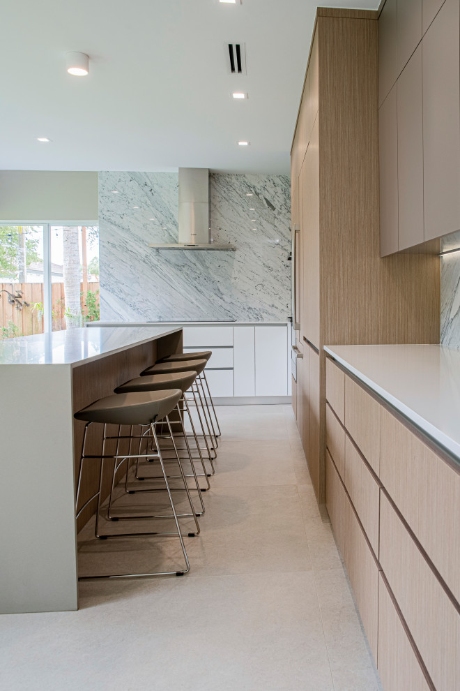 This is an example of a large modern u-shaped eat-in kitchen in Miami with an undermount sink, flat-panel cabinets, light wood cabinets, quartz benchtops, grey splashback, marble splashback, panelled appliances, porcelain floors, with island, beige floor and white benchtop.