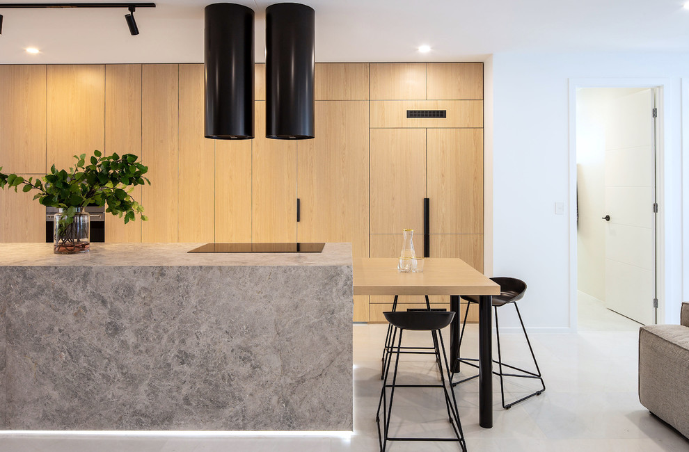 This is an example of a mid-sized modern galley kitchen pantry in Brisbane with an undermount sink, beaded inset cabinets, light wood cabinets, limestone benchtops, grey splashback, black appliances, marble floors, with island, white floor and grey benchtop.