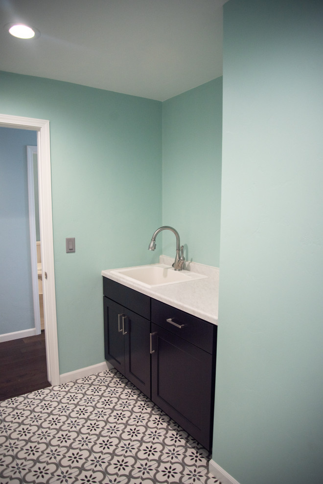 Photo of a large modern dedicated laundry room in Other with a drop-in sink, flat-panel cabinets, black cabinets, laminate benchtops, green walls, ceramic floors, a side-by-side washer and dryer, multi-coloured floor and white benchtop.