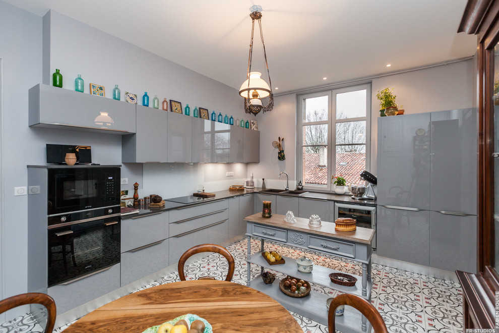This is an example of a large eclectic l-shaped eat-in kitchen in Toulouse with an undermount sink, flat-panel cabinets, grey cabinets, quartzite benchtops, white splashback, glass tile splashback, black appliances, cement tiles and no island.