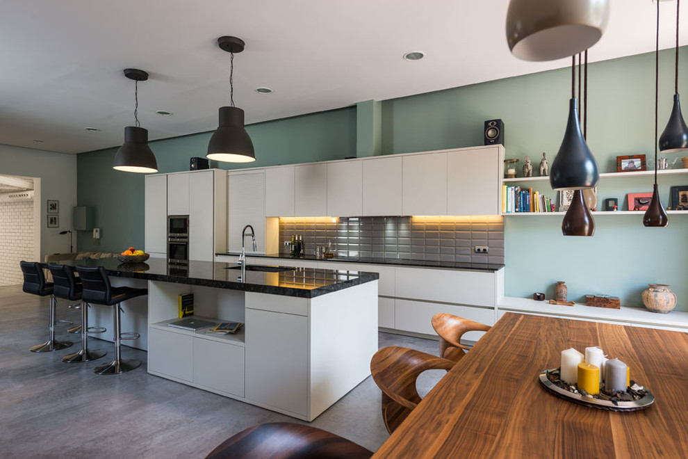 This is an example of a large industrial single-wall open plan kitchen in Barcelona with a single-bowl sink, flat-panel cabinets, white cabinets, marble benchtops, grey splashback, porcelain splashback, stainless steel appliances, concrete floors, with island and grey floor.
