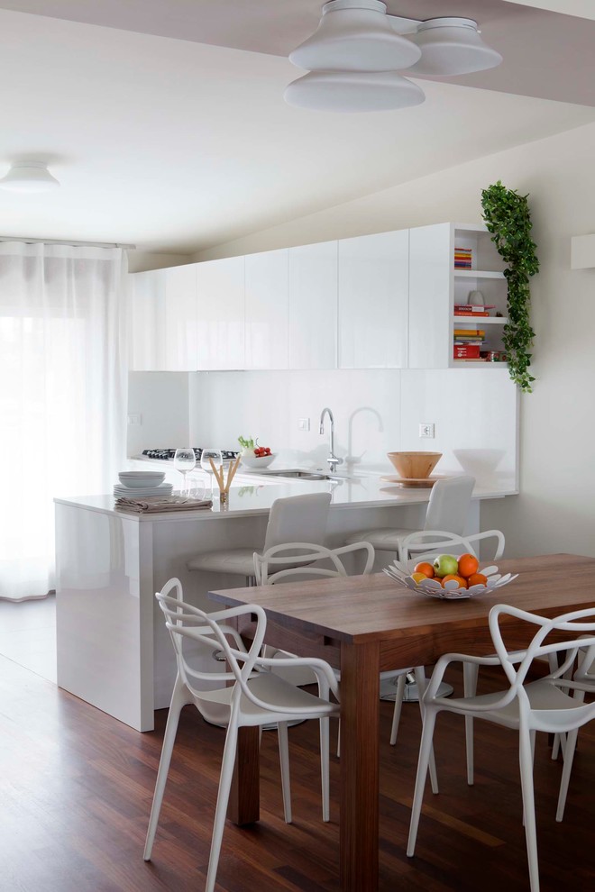 Mid-sized contemporary l-shaped eat-in kitchen in Milan with a drop-in sink, flat-panel cabinets, white cabinets, solid surface benchtops, white splashback and medium hardwood floors.