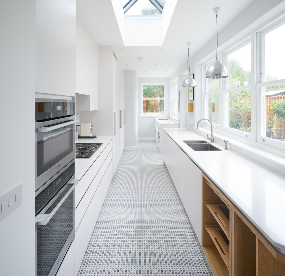 This is an example of a large contemporary separate kitchen in London with an integrated sink, white cabinets, white splashback, stainless steel appliances, porcelain floors and no island.