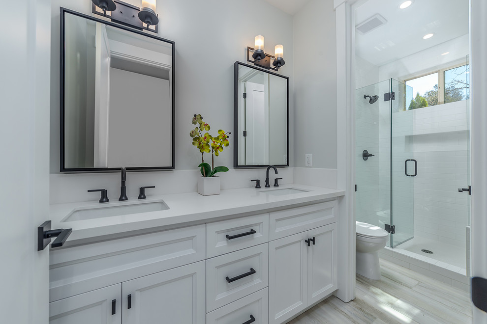 This is an example of a small country 3/4 bathroom in Sacramento with beaded inset cabinets, white cabinets, a freestanding tub, a corner shower, a two-piece toilet, white tile, ceramic tile, grey walls, light hardwood floors, an integrated sink, granite benchtops, grey floor, a hinged shower door and white benchtops.