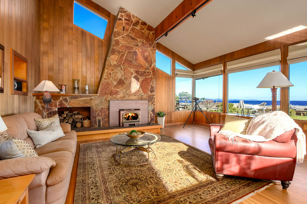 Inspiration for a large beach style open concept living room in Seattle with medium hardwood floors, a wood stove, a stone fireplace surround, brown walls and brown floor.