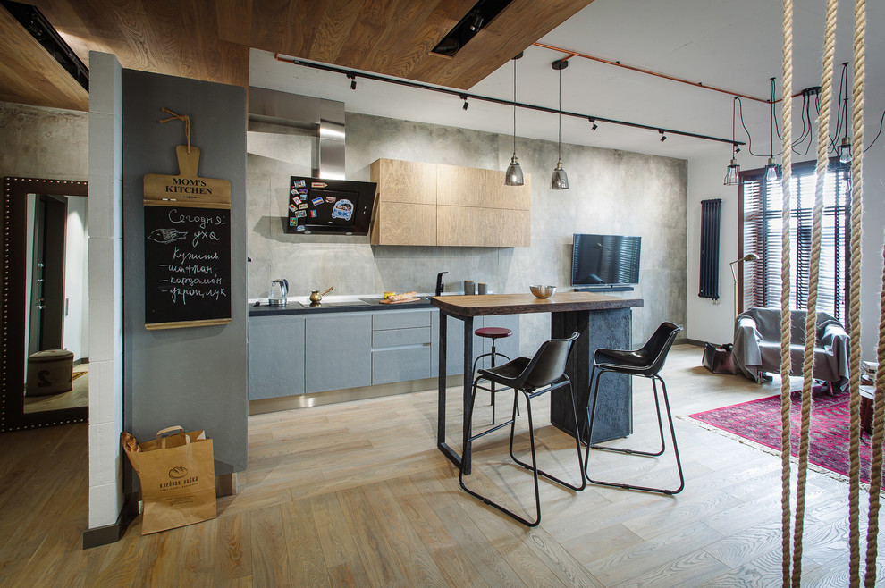 Photo of an industrial l-shaped open plan kitchen in Other with flat-panel cabinets, grey cabinets, grey splashback, light hardwood floors and with island.