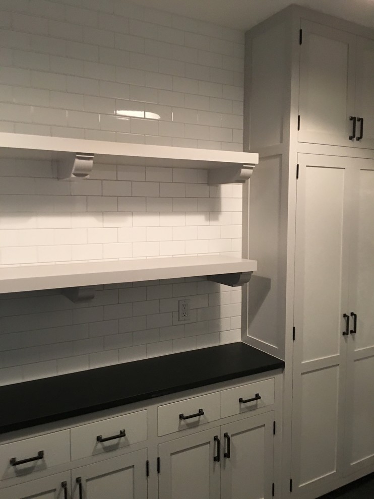 Design ideas for a mid-sized transitional single-wall dedicated laundry room in New York with recessed-panel cabinets, white cabinets, solid surface benchtops, white walls, a stacked washer and dryer and slate floors.