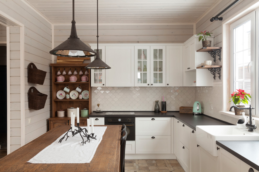 This is an example of a scandinavian l-shaped kitchen in Moscow with a farmhouse sink, shaker cabinets, white cabinets, white splashback, black appliances, with island and brown floor.
