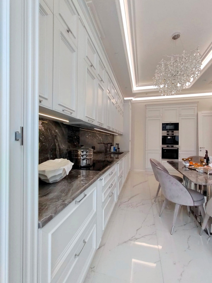 Aménagement d'une grande cuisine américaine linéaire classique avec un évier 2 bacs, un placard avec porte à panneau encastré, des portes de placard blanches, un plan de travail en quartz modifié, une crédence noire, une crédence en quartz modifié, un électroménager en acier inoxydable, un sol en carrelage de porcelaine, un sol blanc et plan de travail noir.