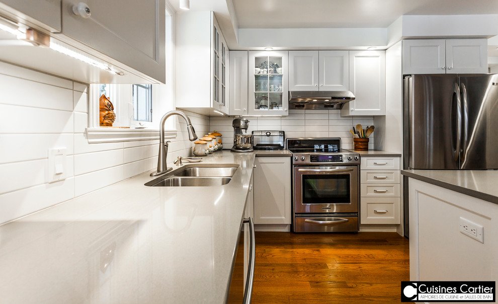 Eat-in kitchen - large transitional medium tone wood floor eat-in kitchen idea in Montreal with a double-bowl sink, shaker cabinets, white cabinets, quartzite countertops, white backsplash, ceramic backsplash, stainless steel appliances and an island
