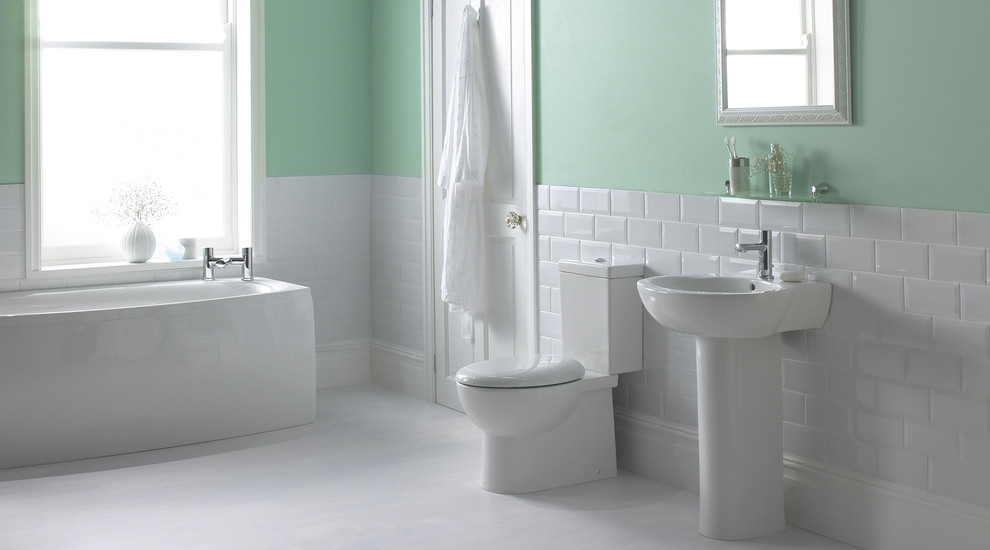 This is an example of a mid-sized contemporary bathroom in Hampshire with a wall-mount sink, a drop-in tub, a one-piece toilet, white tile, green walls and linoleum floors.