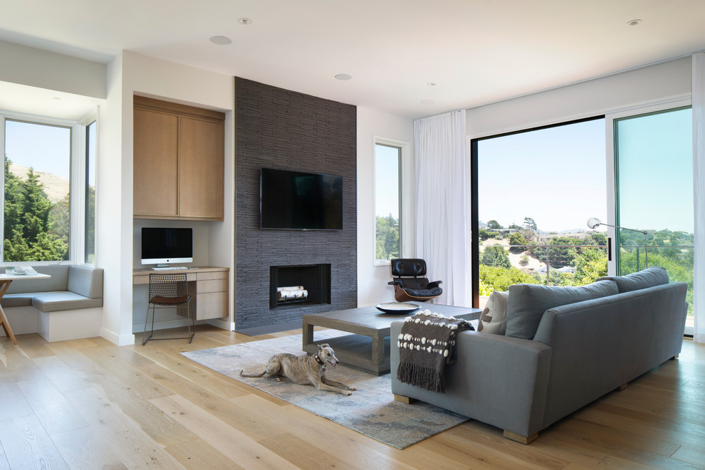 This is an example of a mid-sized contemporary open concept living room in San Francisco with white walls, light hardwood floors, a standard fireplace, a stone fireplace surround, beige floor and a wall-mounted tv.