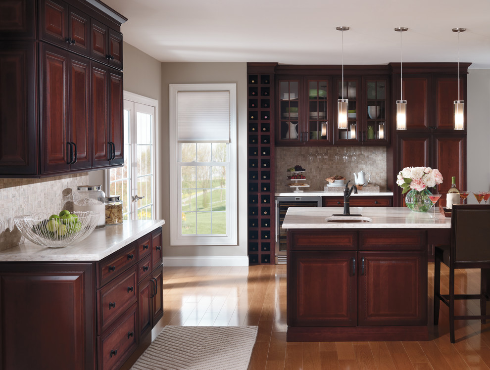 Inspiration for a mid-sized transitional l-shaped eat-in kitchen in Boston with raised-panel cabinets, dark wood cabinets, stainless steel appliances, medium hardwood floors, with island, an undermount sink, granite benchtops, grey splashback, mosaic tile splashback and brown floor.