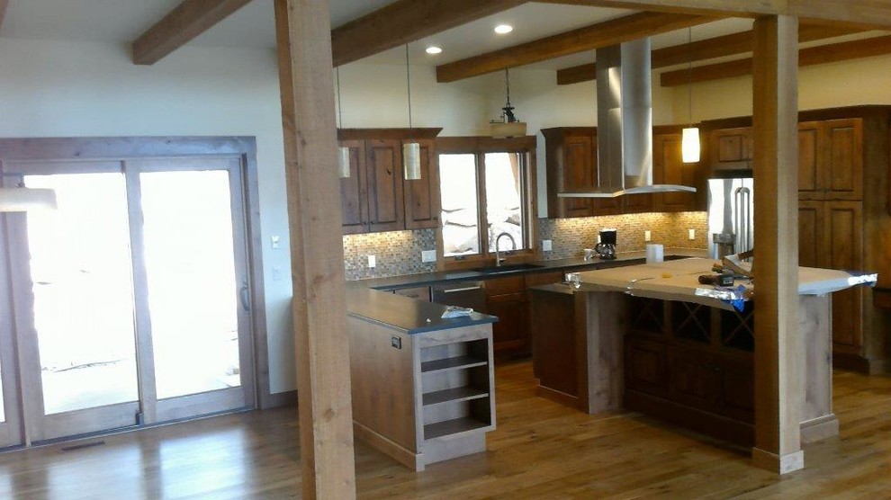 Open concept kitchen - large rustic u-shaped medium tone wood floor and brown floor open concept kitchen idea with an undermount sink, raised-panel cabinets, dark wood cabinets, multicolored backsplash, glass tile backsplash, stainless steel appliances and an island
